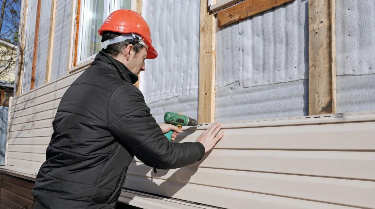 Siding replacement professional using a power drill to install new tan vinyl siding on a home exterior in Stockton, CA